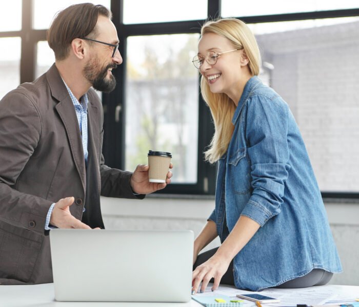 Happy businessman shows done project to his female partner, says that everything is okay, suggests to have coffee break. Two copywriters glad finish work, have great achievements, look in laptop